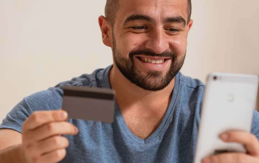 Smiling man holding a credit card and smartphone, highlighting the convenience of mobile eCommerce for online shopping.